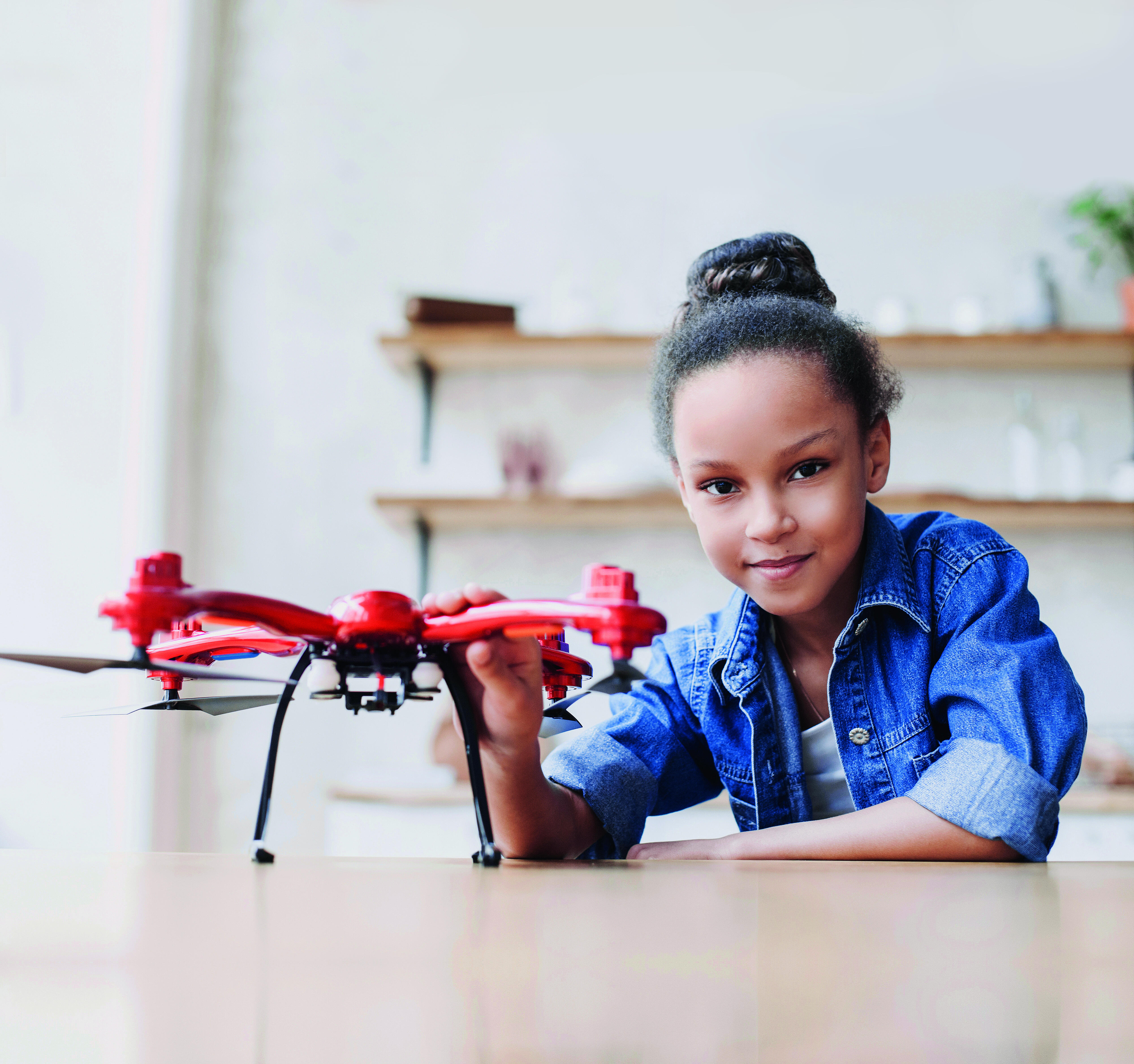 Ein Mädchen sitzt an einem Tisch, vor ihr steht eine Drohne. Bei dem Bild handelt es sich um das Key Visual Motiv des Ada-Lovelace-Projekts Rheinland-Pfalz