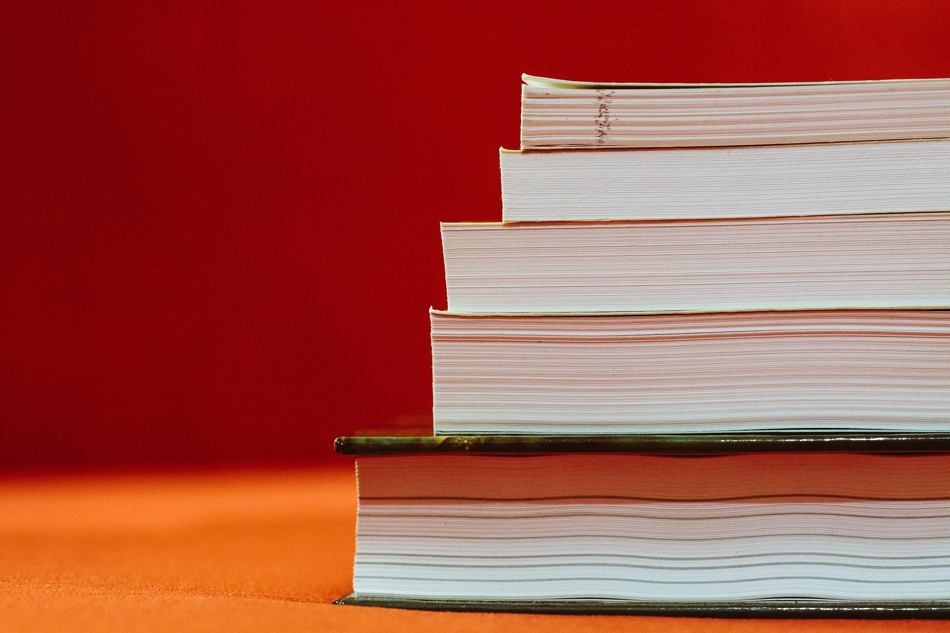 Ein Stapel Bücher oder Studien vor orangenem Hintergrund.